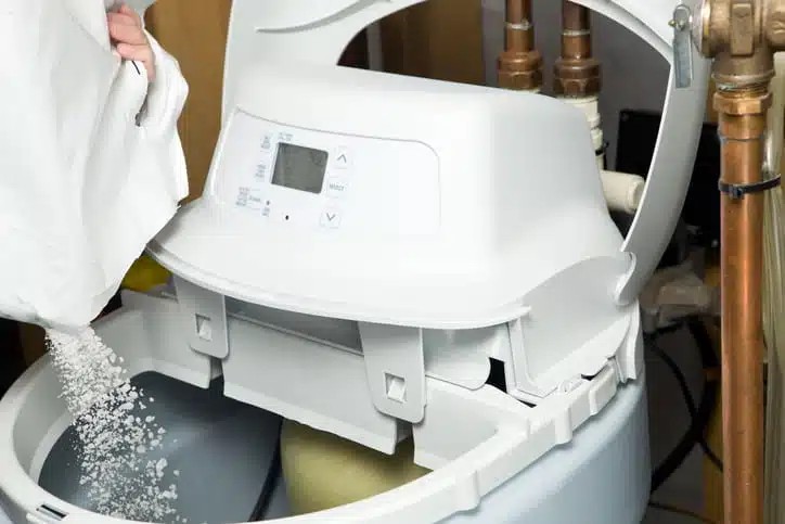 A person pouring water softener salt into their water softening system.